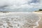 Woman walks along beach at high tide under stormy sky with turbulent ocean