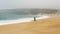 Woman walks along beach washed by stormy ocean against hill