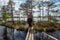 A woman walks along wooden walkways near a small lake.