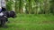 A woman walks a black labradoodle dog from left to right along a country track through a leafy green forrest