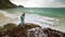 Woman walks on rock of sea reef stone, stormy cloudy ocean. Blue swimsuit dress tunic. Concept rest, tropical resort