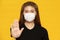 Woman waring protection mask from coronavirus and air pollution making stop hand sign isolated on yellow background