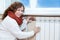 Woman in warm clothes checking the temperature of heating radiator in room