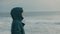 A woman in a warm jacket with a hood on her head, looking at the ocean and the waves. Side view. Travel and recreation