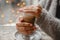 A woman in a warm jacket is sitting at a table by the window and warms her hands on coffee on the bokeh bakground