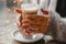 A woman in a warm jacket is sitting at a table by the window and warms her hands on coffee on the bokeh bakground