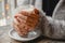 A woman in a warm jacket is sitting at a table by the window and warms her hands on coffee on the bokeh bakground