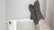 A woman warms her frozen feet in woolen warm socks on a home heater radiator