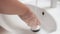 A woman washes her hands in the sink with soap.