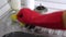 Woman washes a metal sink with sponge in the kitchen in red gloves. Hands close-up.