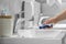 Woman washing electric toothbrush under flowing water from faucet in bathroom, closeup