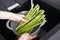 Woman washing fresh raw asparagus over sink