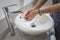 Woman washing her hands in a white round sink in the bathroom