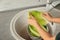 Woman washing leaf of savoy cabbage under tap water in kitchen sink