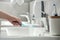 Woman washing plastic toothbrush under flowing water from faucet in bathroom, closeup