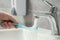 Woman washing plastic toothbrush under flowing water from faucet in bathroom, closeup