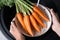 Woman washing ripe carrots in colander with running water over sink, closeup