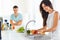 Woman washing vegetables in the sink and man standing next to he