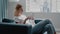 Woman watches social media on mobile phone on sofa by window