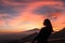 Woman watching beautiful sunset behind volcano Mount Etna near Castelmola, Taormina, Sicily. Clouds with vibrant red orange colors