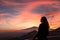 Woman watching beautiful sunset behind volcano Mount Etna near Castelmola, Taormina, Sicily. Clouds with vibrant red orange colors