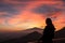Woman watching beautiful sunset behind volcano Mount Etna near Castelmola, Taormina, Sicily. Clouds with vibrant red orange colors