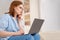 Woman watching webinar at computer on couch.