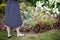 A woman waters flowers in her garden with a steel watering can.