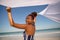 Woman waving white scarf in wind on beach in the sunshine