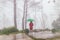 Woman wear red coat opened green umbrella turn back with fog