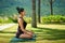 Woman wearing active wear doing yoga practice meditating in park nature, lotus position. Meditation in sunny day, inner balance