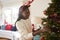 Woman Wearing Antlers Hanging Decorations On Christmas Tree At Home