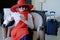 Woman wearing the big red hat with suitcase checking out of hotel with her baggage sitting on bed waiting for taxi ordered on