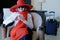 Woman wearing the big red hat with suitcase checking out of hotel with her baggage sitting on bed waiting for taxi ordered on