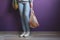 woman wearing casual clothes holding string shopper bag with fresh fruits and a pineapple against violet wall, eco friendly