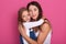 Woman wearing casualo clothes have fun with cute child baby girl. Mommy and her little kid daughter posing isolated over pink