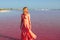 Woman wearing elegant summer dotted dress walking at bang of salty pink lake with crystals of salt