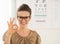 Woman wearing eyeglasses showing ok gesture near Snellen chart