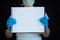 Woman wearing face mask and surgical gloves, holding blank note pad with black background