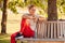 Woman Wearing Fitness Clothing Sitting On Seat Under Tree Checking Activity Monitor On Smartwatch