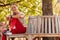 Woman Wearing Fitness Clothing Sitting On Seat Under Tree Checking Activity Monitor On Smartwatch