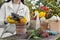 Woman wearing gardening gloves transplanting flower into pot at wooden table outdoors, closeup