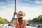 A woman wearing a hat stands in front of the majestic Eiffel Tower, tourist woman in summer dress and hat standing on beautiful