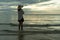 Woman wearing a hat walks alone on an empty sandy beach at sunset. A lonely and depressed young woman stands on the sand of the be