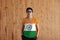 Woman wearing India flag color shirt and standing with two hands in pant pockets on the wooden wall background