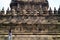 A woman wearing a long-sleeved shirt is taking a photo of the reliefs of the Prambanan temple