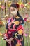 Woman wearing a mask in kimono in front of a wall of flowers