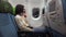 Woman wearing medical mask takes off it on chin sitting in airplane and turning off smartphone