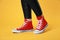 Woman wearing pair of new stylish sneakers on yellow background, closeup