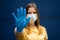 Woman wearing protective face mask, focused on outstretched hand with protection glove as stop symbol. Corona virus